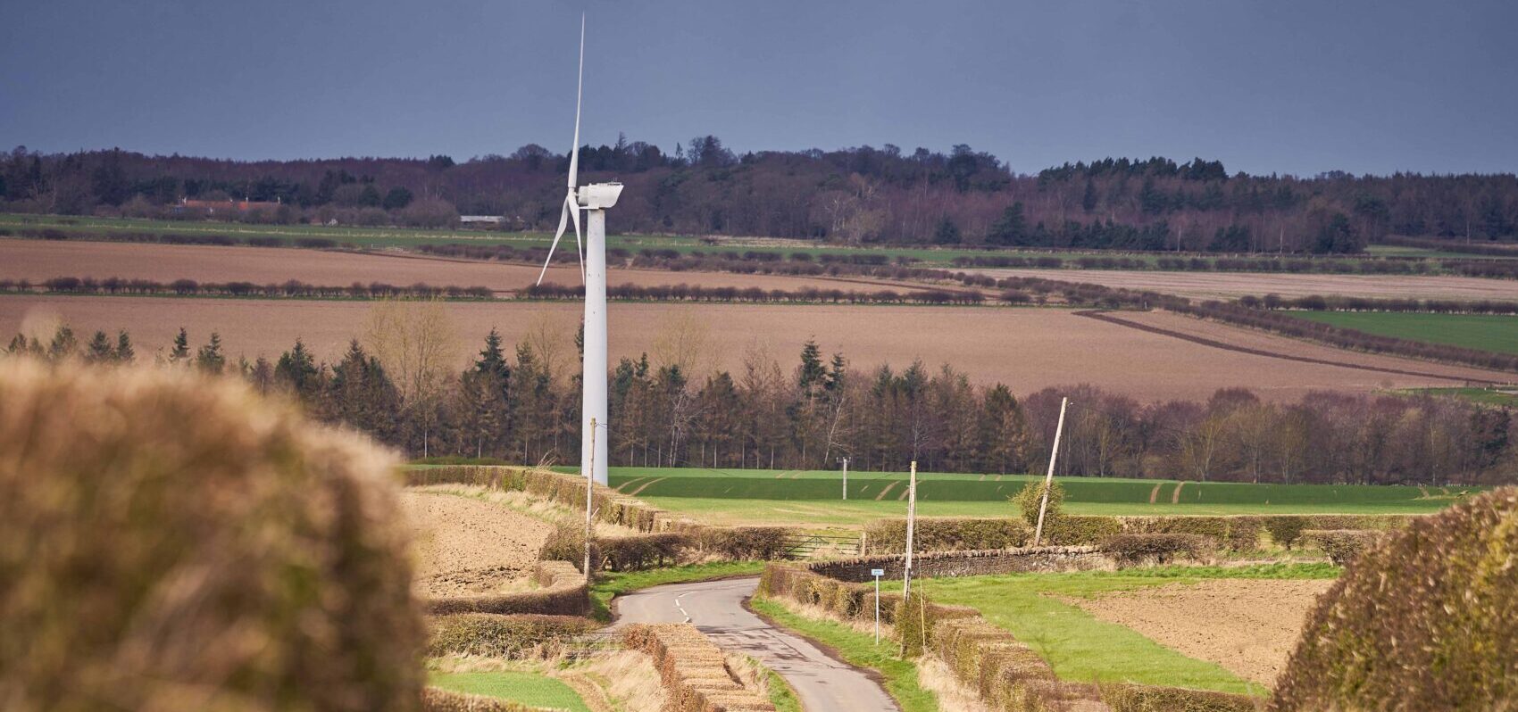 Rural landscape featuring hay bales, wind turbine and winding road